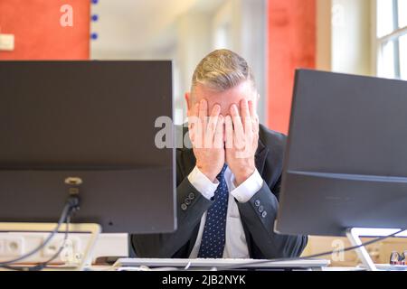 Stressato uomo d'affari con le mani davanti agli occhi seduti al computer in ufficio Foto Stock