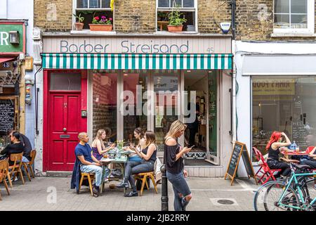 Persone seduti fuori Barber Streisand un barbiere unisex offbeat sul mercato Exmouth, Clerkenwell, Londra EC1 Foto Stock