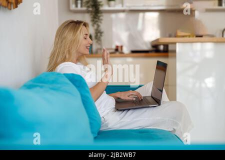 Bella donna caucasica allegra ondeggiando con la mano alla webcam e avendo video chat sul computer. Foto Stock