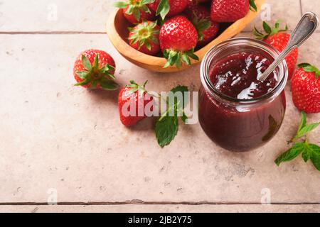 Marmellata di fragole. Marmellata di fragole in vaso di vetro con piatto di frutti di bosco freschi su un vecchio sfondo di tegole spaccate, primo piano. Marmellata di fragole fatte in casa. Foto Stock