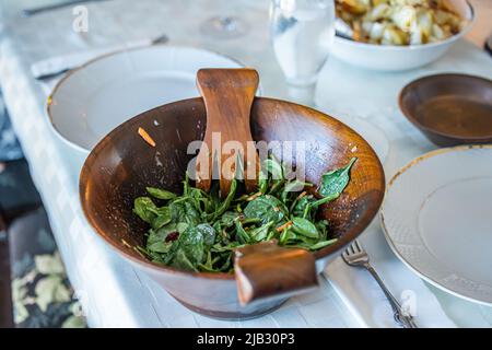 Un'insalata di spinaci verdi in una rustica ciotola di insalata di legno seduta su un tavolo a cena Foto Stock