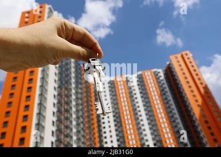 Casa chiavi in mano maschile sullo sfondo di nuovi edifici residenziali. Agente immobiliare, casa in movimento o affitto di proprietà Foto Stock