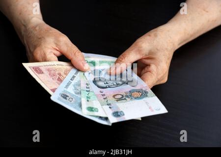 Donna anziana con banconote yuan in mani ruggite. Concetto di pagamenti pensionistici in Cina, risparmio al pensionamento, pensionato cinese con denaro Foto Stock