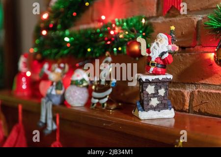 Decorazione natalizia sul mantello di una stufa a legna, con alcune luci colorate accese. Il punto focale è specifico in uno degli elementi della decorazione Foto Stock