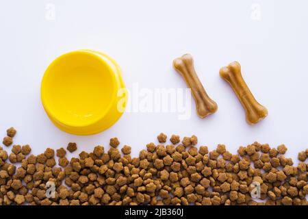 vista dall'alto dei trattamenti per cani a forma di osso vicino a ciotole di plastica e alimenti per animali domestici Foto Stock