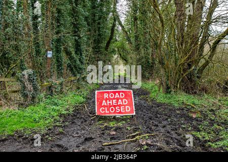 Strada davanti al segnale di avvertimento di traffico chiuso su strada fangosa nella campagna di Cheshire Foto Stock