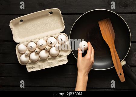 uova di pollo in scatole e testo 2022 sulle uova, felice anno nuovo 2022, uova di pollo sul tavolo e padella, uova strapazzate frittura Foto Stock