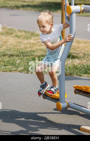 Il ragazzino gioca con un'attrezzatura da palestra all'aperto. Foto Stock