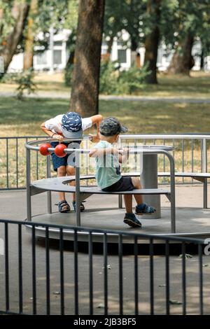 Due bambini su un carosello per bambini in metallo che gira intorno. Foto Stock