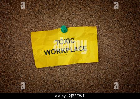 Una nota appiccicosa sbriciolata con le parole Toxic Workplace su di essa fissata a un pannello di sughero. Primo piano. Foto Stock