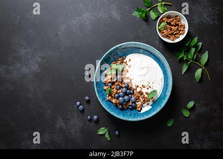 Granola al cioccolato con yogurt bianco semplice e mirtillo fresco in una ciotola, cibo sano per la prima colazione, vista dall'alto Foto Stock