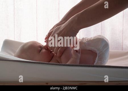 Madre che fa il massaggio alla sua bambina che raggruppa le gambe alla testa. Stile di vita sano dall'inizio della vita Foto Stock