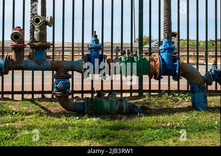 I tubi dell'acqua industriali con valvole e raccordi dei tubi flessibili sono situati sopra il suolo nel parco. Primo piano. Foto Stock