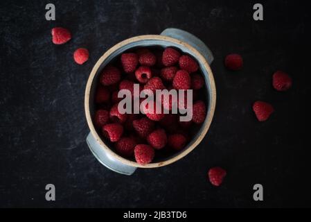 Ciotola di lamponi in ciotola di ceramica fatta a mano su sfondo scuro. Foto Stock