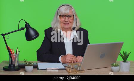 Donna d'affari anziana indossa cuffie wireless per videochiamare in conferenza sul laptop. Donna anziana professionale call center agentoperator avere distanza webcam chat lavoro intervista sul computer in ufficio Foto Stock