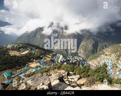 Namche Bazaar visto dai passi vertiginosi che portano a Syangboche. Il Centro visitatori del Parco Nazionale Sagarmatha si trova sulla collina boschiva sulla sinistra. Foto Stock