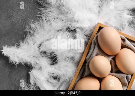 Scatola con uova e belle piume su sfondo grigio Foto Stock