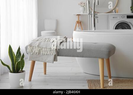 Panca morbida vicino alla vasca da bagno nella stanza luminosa Foto Stock