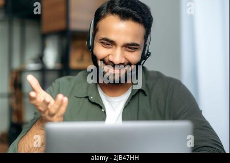 Operatore positivo di call center arabo o indiano, consulente hotline, mentore, con cuffie, tenendo una consultazione online con i clienti o una conferenza online con lo studente, parlando con videochiamata, sorridendo Foto Stock