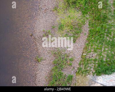 Riva del fiume da sopra texture sfondo. Vista dall'alto su una transizione naturale dall'acqua alla terra. Pietre di ciottoli sott'acqua ed erba. Foto Stock