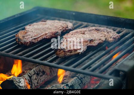 Fuoco selettivo di succose bistecche di manzo grigliate su griglia barbecue con fumo Foto Stock