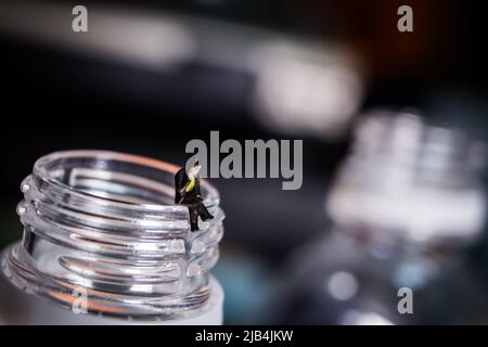 Uomo d'affari in miniatura seduto sul collo della bottiglia di plastica. L'uomo nell'immagine sta effettuando una chiamata telefonica con il suo telefono cellulare. Foto Stock