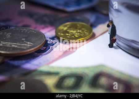 L'uomo d'affari in miniatura in piedi vicino alla carta trasparente weghit con banconote e monete sul tavolo bianco in umore spooky. Foto Stock