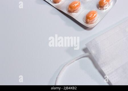 Maschera facciale bianca semplice (copertura) con pillole su sfondo bianco. Foto Stock