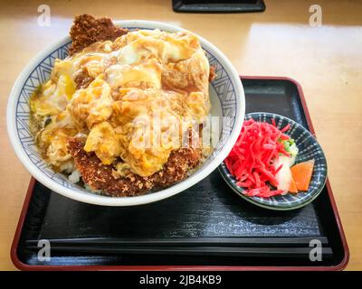 Katsudon, una ciotola di riso con una cotoletta di maiale fritta, uova, verdure e condimenti, con sottaceti Tsukemono in un ristorante locale in Giappone. Foto Stock