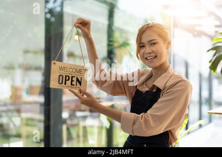 Il proprietario del negozio che apre il cartello attraverso il vetro della porta e pronto per l'assistenza. Felice asiatico femmina concetto di piccola impresa Foto Stock