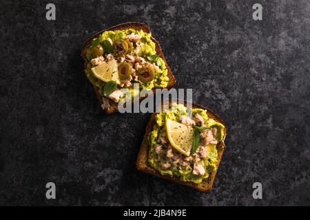 Preparare gustosi toast al tonno. Bruschetta italiana con tonno in scatola, avocado, olive, deliziosa prima colazione o snack. Vista dall'alto. Foto Stock