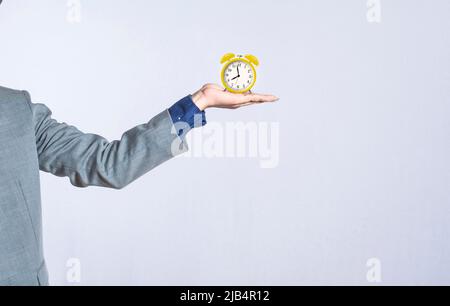 Una mano che tiene un orologio da tavolo su sfondo isolato, primo piano di una mano che tiene una sveglia, uomo d'affari mano che tiene orologio isolato Foto Stock