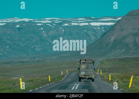 Vista posteriore di un'avventura fuoristrada che viaggia attraverso le strade islandesi verso le montagne. Viaggio su strada epico con un'auto o un veicolo in atterraggio. Foto Stock