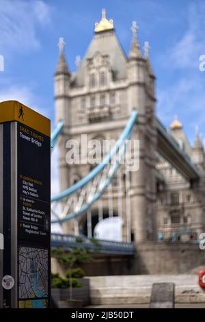 LONDRA, UK - 01 GIUGNO 2022: Ufficio informazioni turistiche con le indicazioni per Tower Bridge e vista sfocata del Tower Bridge sullo sfondo Foto Stock