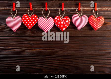 Cuori di tessuto valentini appesi su corda su sfondo di legno scuro Foto Stock