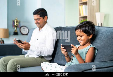 Padre e figlia sul divano sono occupati separatamente utilizzando il telefono cellulare a casa - concetto di digital divide, social media e dipendenza dalla tecnologia Foto Stock