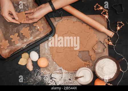 Cucinare i biscotti di Natale del pan di zenzero su uno sfondo scuro. Tagliare il pan di zenzero dall'impasto utilizzando uno stampo per pan di zenzero, vista dall'alto, pasta cruda con cinna Foto Stock