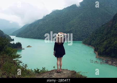 Una ragazza in un cappello e un vestito si erge su una pietra sullo sfondo del serbatoio di Ingur a Svaneti. Montagne del Caucaso in estate Foto Stock