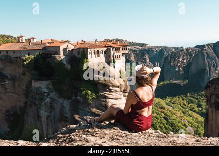 Giovane donna si siede indietro per la fotocamera sulla sommità del monte e guarda alla valle e rocce. Nozione di viaggio, la felicità, la libertà. Traveler enjoyin Foto Stock