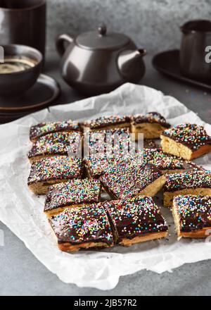 Deliziosa torta fatta in casa con glassa al cioccolato fondente e zucchero colorato cospargere su carta da forno. Stile rustico. Messa a fuoco selettiva. Foto Stock