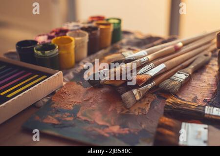 Foto con angolo di visualizzazione della tavolozza con vernici a olio misto, gouache, pastelli e pennelli impostati in studio d'arte Foto Stock