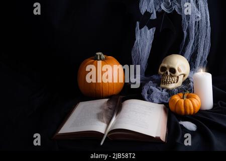 un cranio, zucche, una bottiglia, una candela, tazze e un libro su un tavolo nero e una zucca levitating e una piuma e una tazza di vino su uno sfondo nero Foto Stock