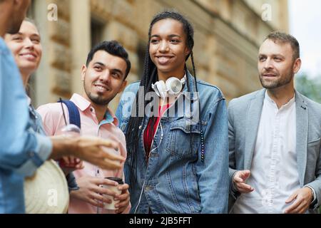 Gruppo di giovani amici multietnici positivi in abiti casual in piedi sulla strada della città e chiacchierare insieme Foto Stock