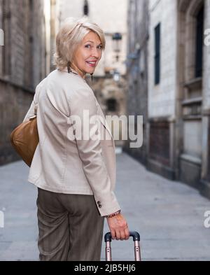 Elegante donna matura è in posa con valigia nel tempo a piedi Foto Stock
