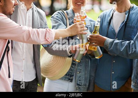 Primo piano di giovani amici eccitati che si alzano in cerchio e si aggraffano le bottiglie mentre bevono birra all'aperto Foto Stock