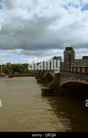 Vista sul Tamigi Londra di colore marrone / colorato e il ponte Lambeth in giornata di sole con le nuvole Foto Stock