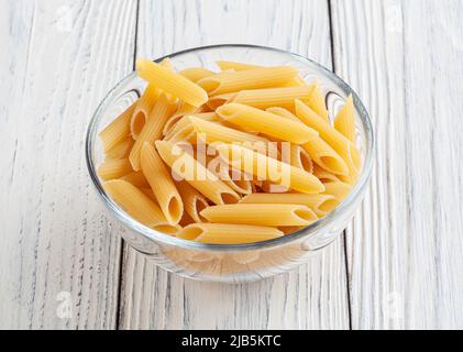 Penne non cotte in ciotola di vetro su tavola di legno bianco Foto Stock