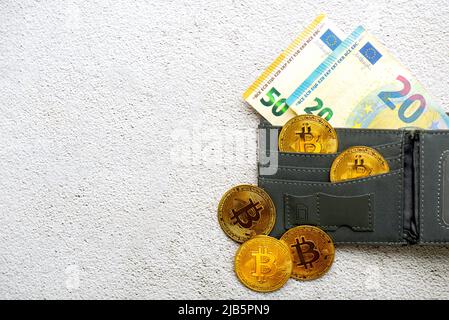 Vista dall'alto delle monete bitcoin d'oro in un portafoglio con bollette in euro sul pavimento. Valuta criptata elettronica Foto Stock