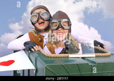 Le sorelle gemelle si siedono ai comandi del loro fantasioso aeroplano. Giocano pilota e co-pilota con un aeroplano fatto da oggetti trovati nel loro giardino. Foto Stock