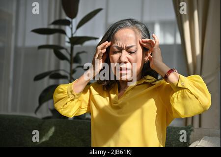 Infelice anziana asiatica con espressione di mal di testa, toccando la testa, avendo emicrania. Concetto di problemi di salute Foto Stock